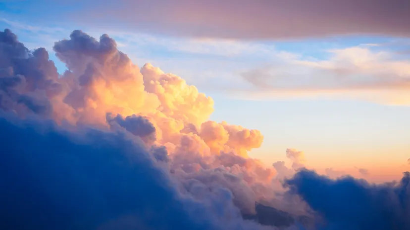 Fluffy clouds illuminated by sunset colors against a blue sky.